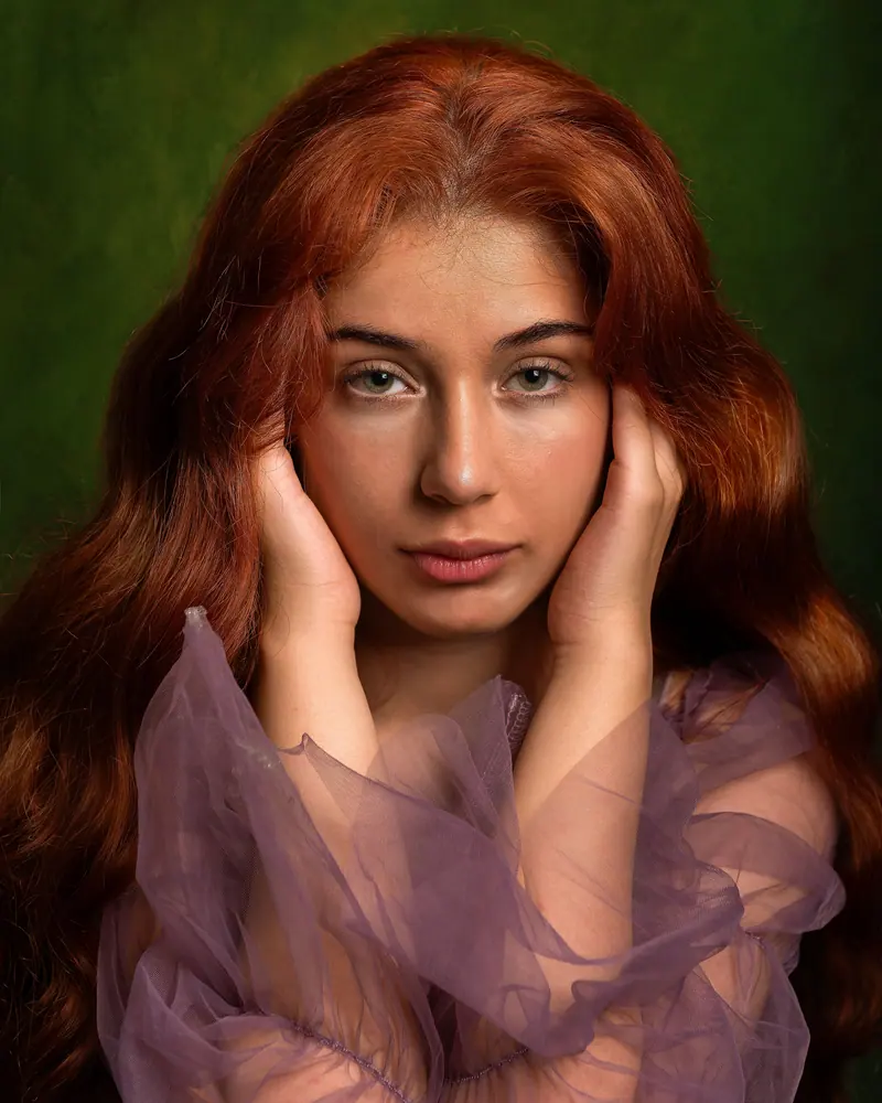 Artistic portrait of a young woman with auburn hair and a pensive expression, in soft purple attire.