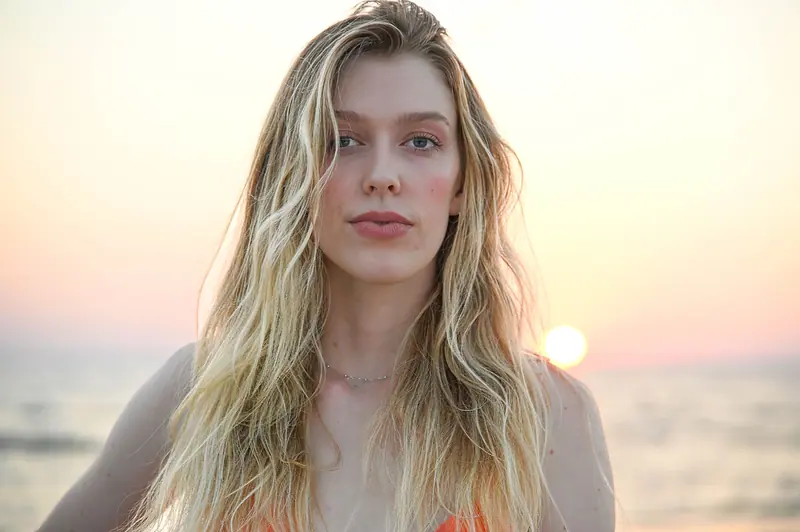 A young woman with flowing hair poses elegantly against a serene beach sunset.