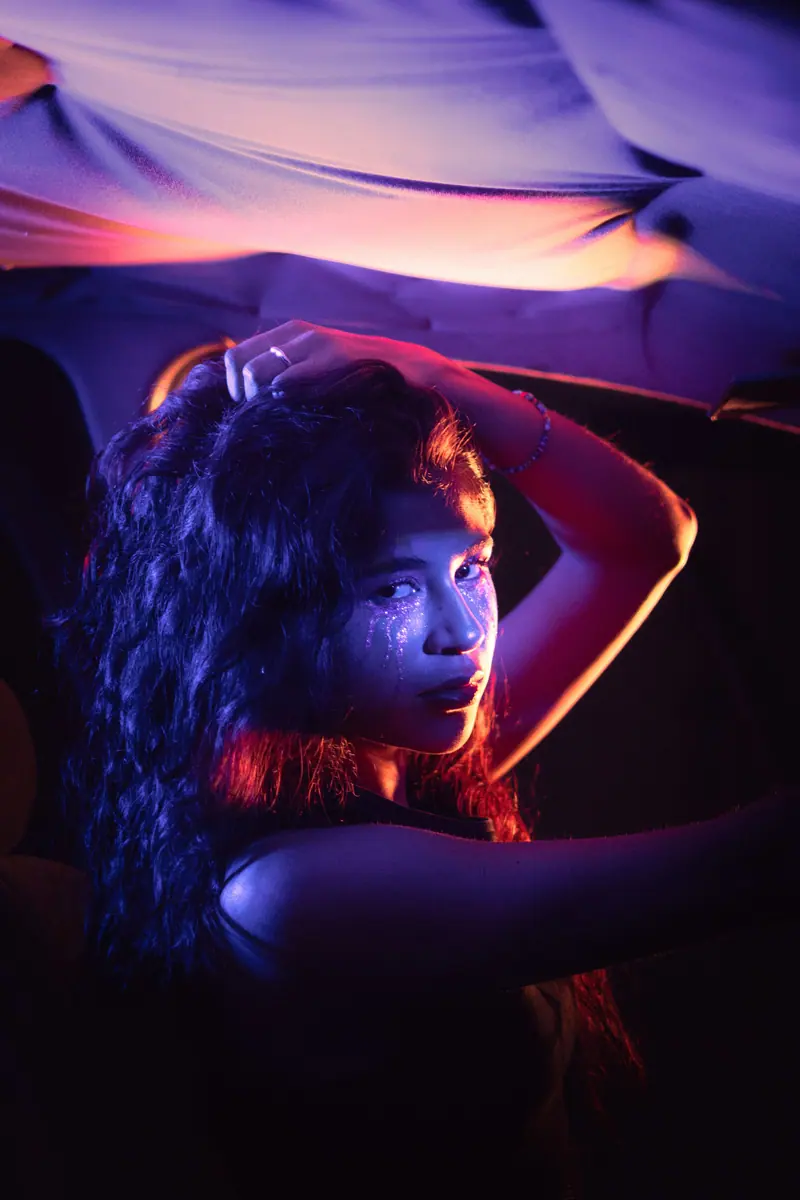 Artistic portrait of a woman illuminated by vibrant neon lights in a car interior.