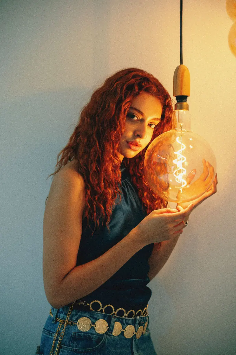 A young woman with curly hair holds a glowing bulb, creating a warm ambiance.
