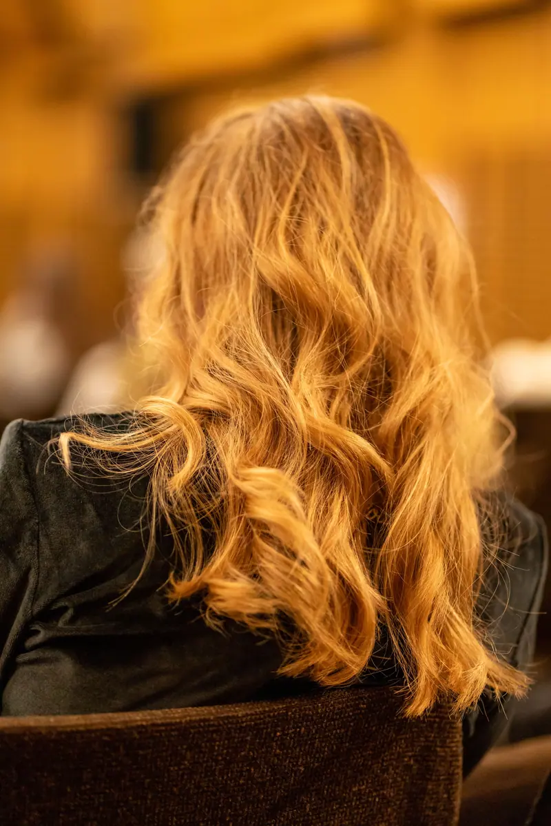 A candid shot from behind of a person with wavy blonde hair in an indoor environment.