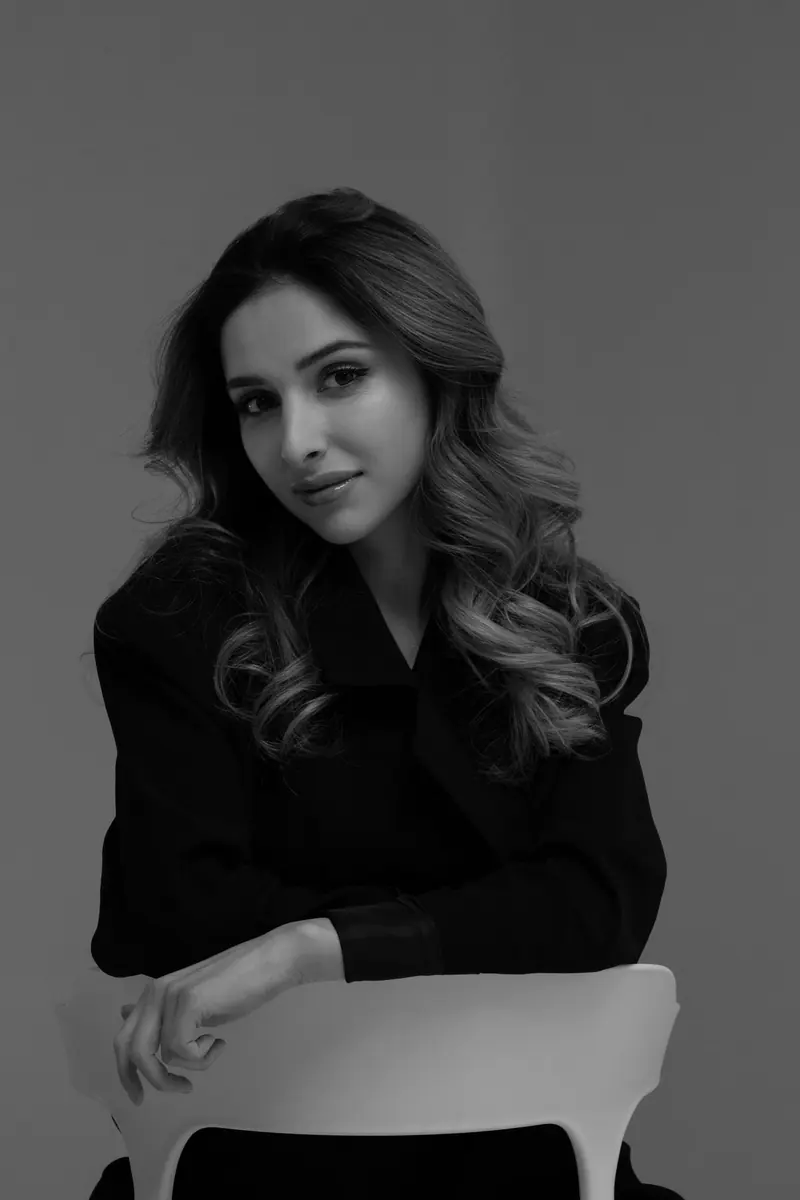 Artistic black and white portrait of a woman with long wavy hair, seated indoors.
