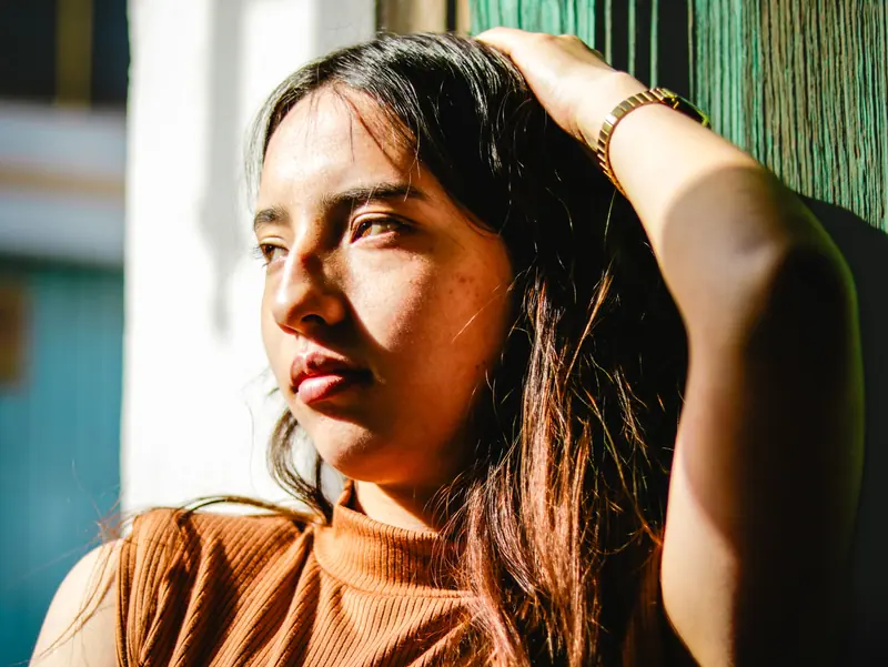 A thoughtful woman gazes out, bathed in warm sunlight, creating a vivid and introspective portrait.