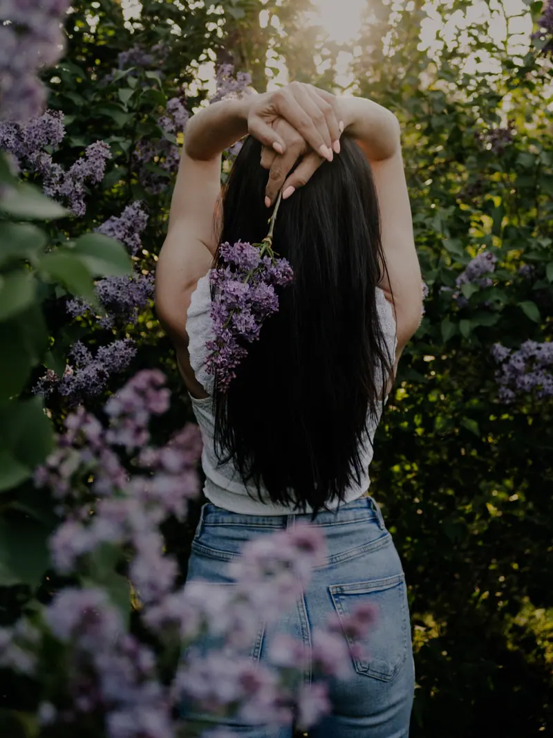 Woman enjoying a floral garden at sunset, arms raised with lavender blooms. Peaceful and natural setting.