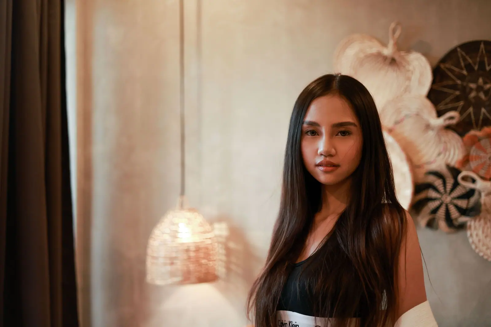 Elegant portrait of a young woman indoors with artistic wall decor and soft lighting.