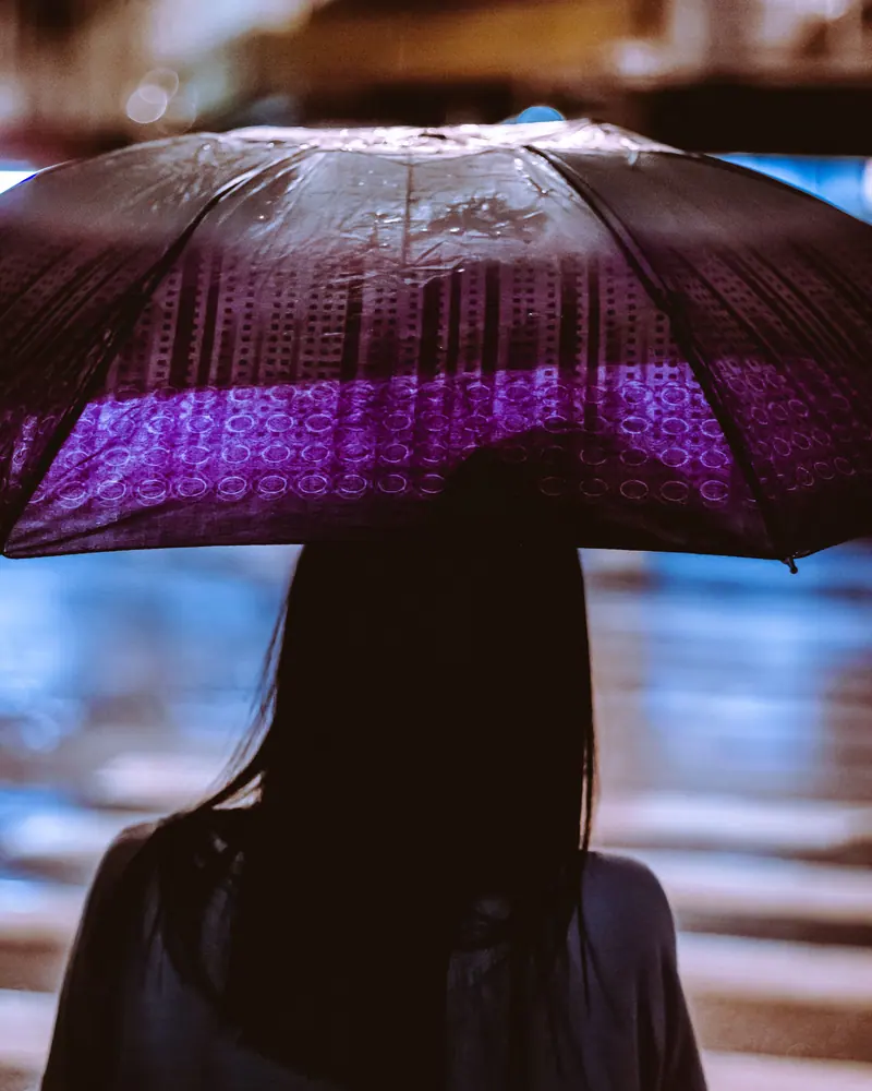 Silhouette of a woman with an umbrella on a rainy night street.