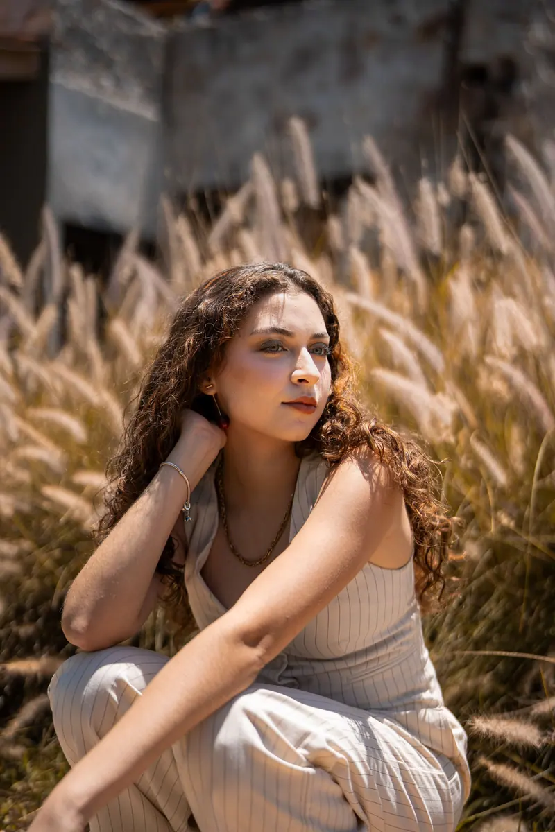 A woman sits in a field of grasses, enjoying a sunny day with a serene expression.