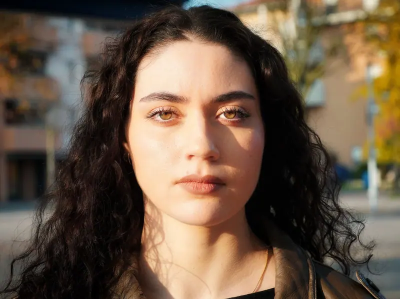 Close-up portrait of a young woman outdoors, with expressive eyes and sunlight highlighting her features.