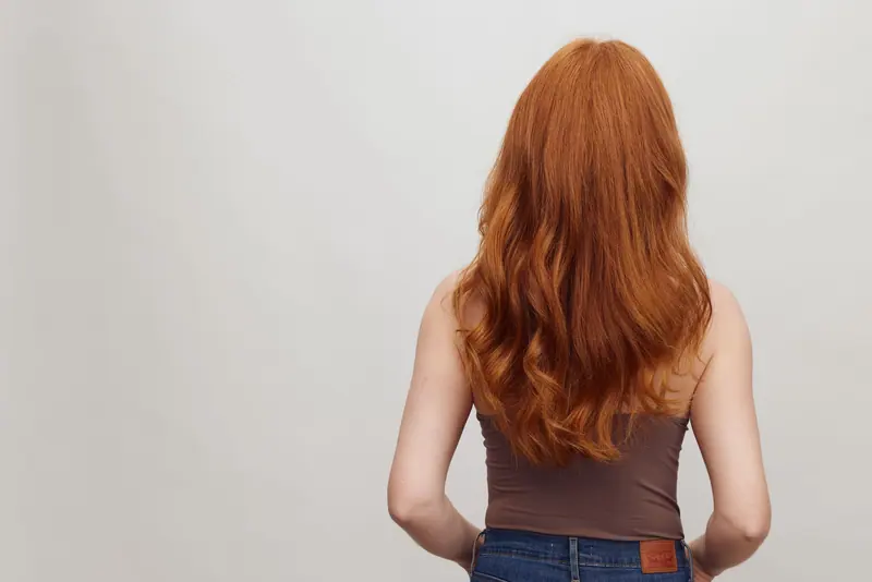 A woman with flowing red hair stands against a plain backdrop in Copenhagen.