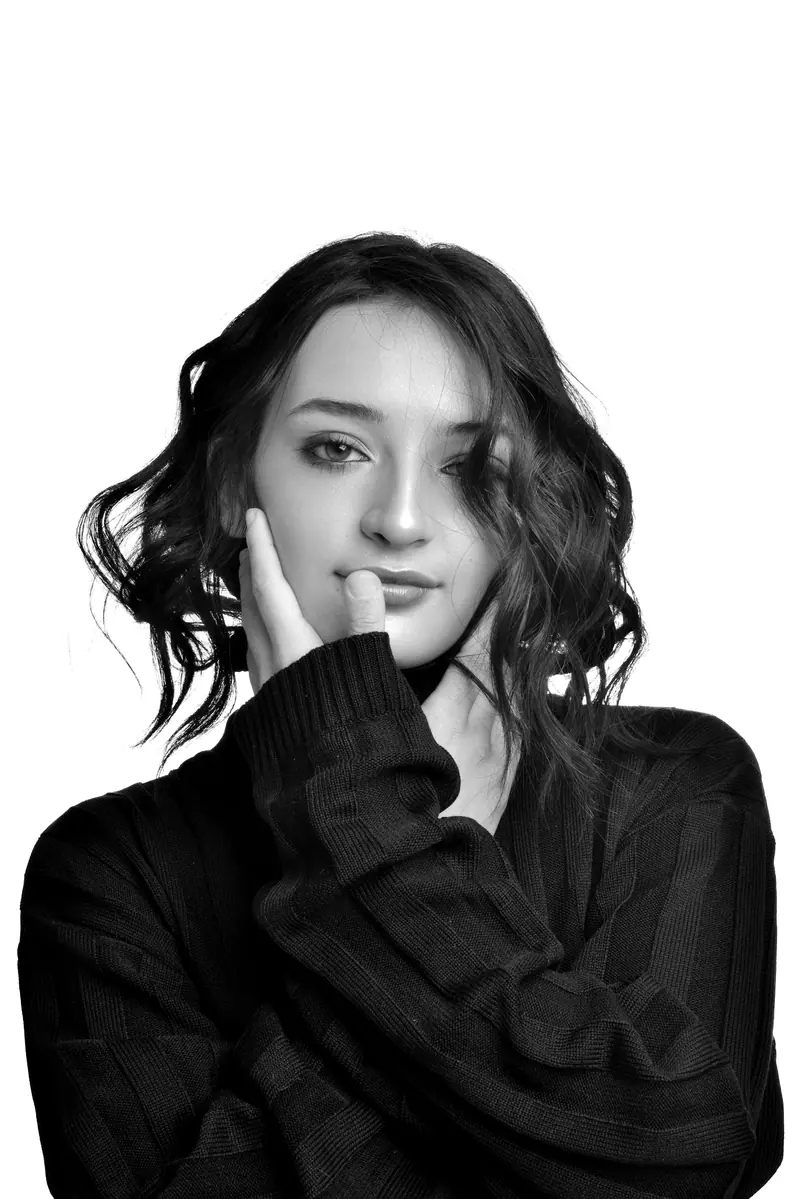 Elegant black and white portrait of a young woman wearing a sweater with wavy hair.