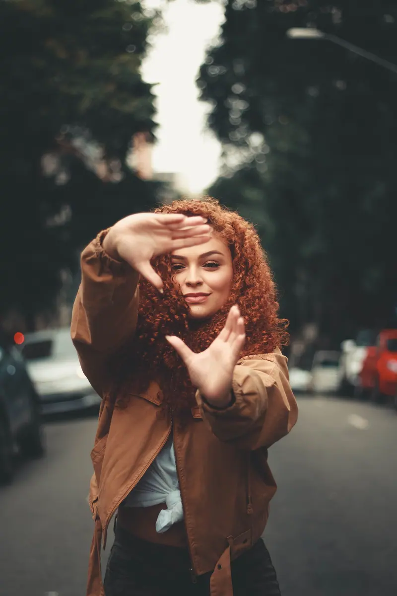 Charming young redhead woman making a playful hand gesture on an urban street.