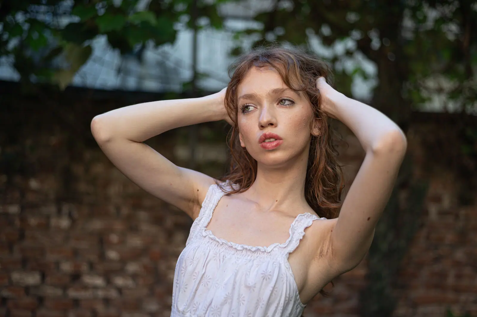 Portrait of a young woman with auburn hair, posing outdoors in a summer setting.