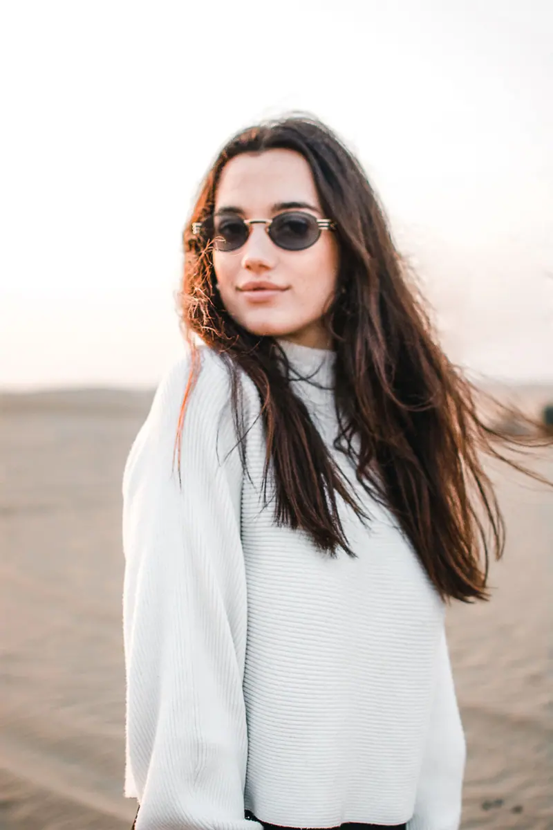 Woman in sunglasses standing on the beach at sunset, exuding style and confidence.