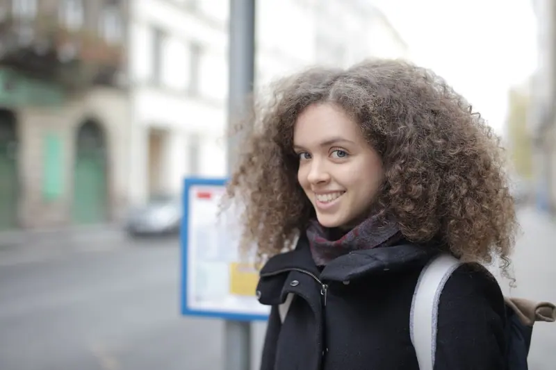 Happy young woman with curly hair walking in the city, enjoying a winter day.