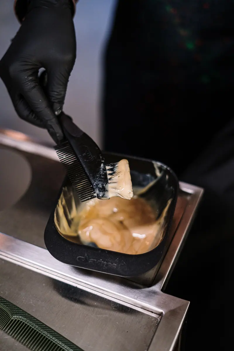 Close-up of stylist mixing hair dye with black brush in salon environment.