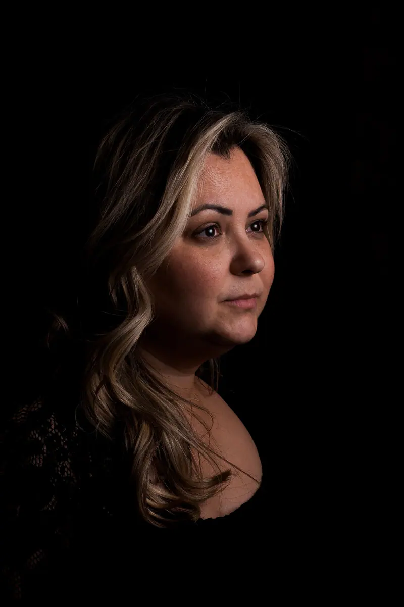 Studio portrait of a woman with wavy hair against a dark background, exuding calmness.