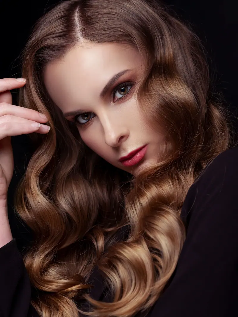 Elegant brunette woman in a close-up fashion portrait with stunning wavy hair and makeup.