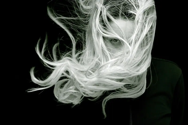 A striking black and white portrait of a woman with long, flowing hair that creates a sense of motion and mystery.