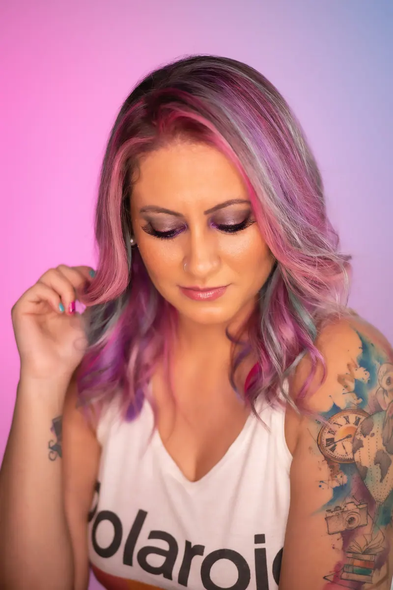 Portrait of a woman with vivid pink and purple hair, showcasing unique tattoos.