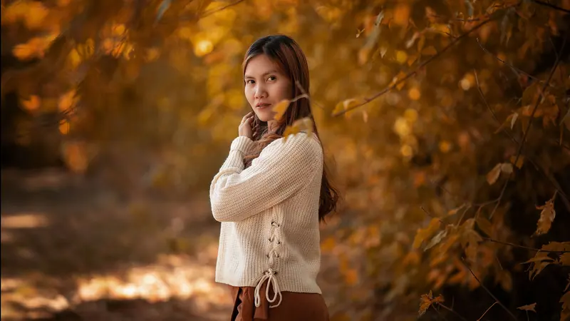 Woman in a knitted sweater surrounded by golden autumn leaves, exuding warmth and tranquility.