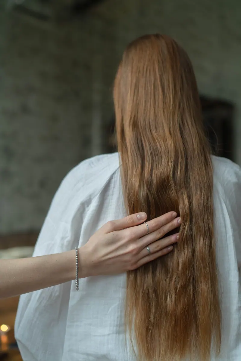 A hand gently touching a woman's long brown hair, creating a serene moment.