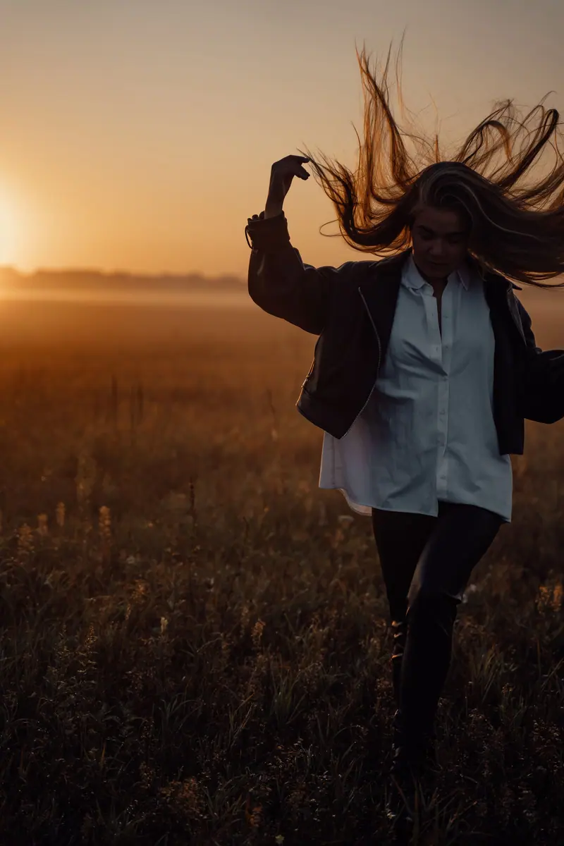 A woman with long hair walks through a foggy field at sunrise, creating a dramatic silhouette.
