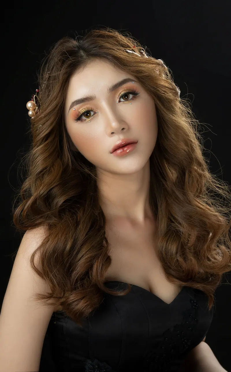 Portrait of an elegant woman with wavy hair and professional makeup, set against a black background.