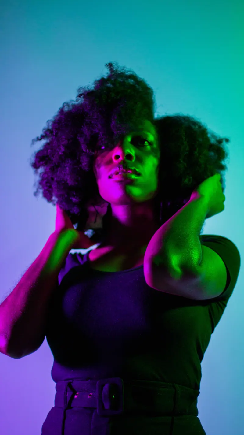 Striking portrait of a woman with curly hair under colorful lighting, showcasing bold and artistic expression.