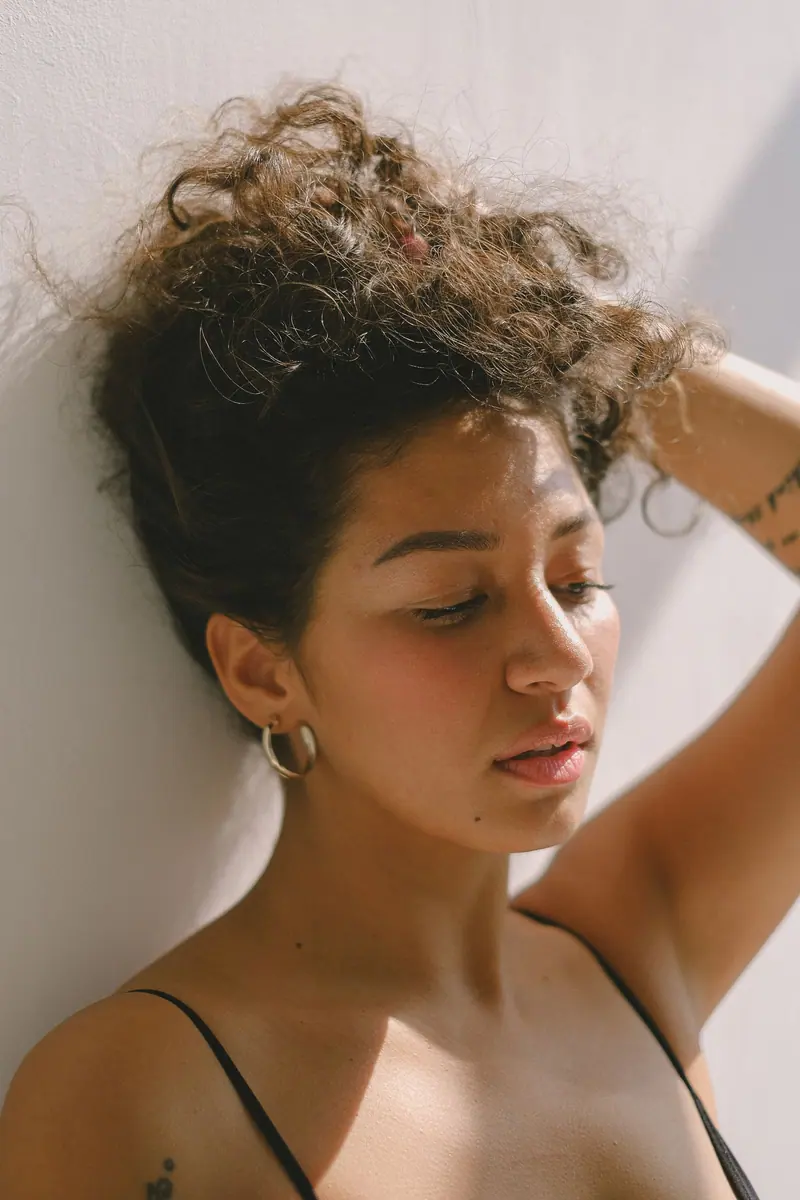 A beautiful portrait of a woman with wavy hair and tattoos against a light background.