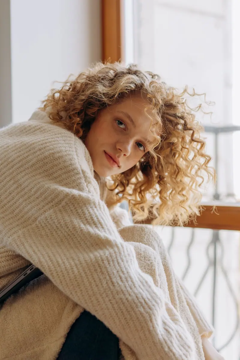 Woman sitting by a window in a warm knitted sweater, capturing a moment of relaxation.