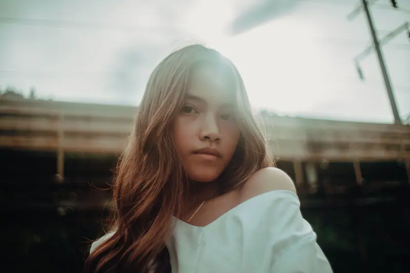 A serene portrait of a young woman in sunlight, blending natural beauty with urban ambiance.