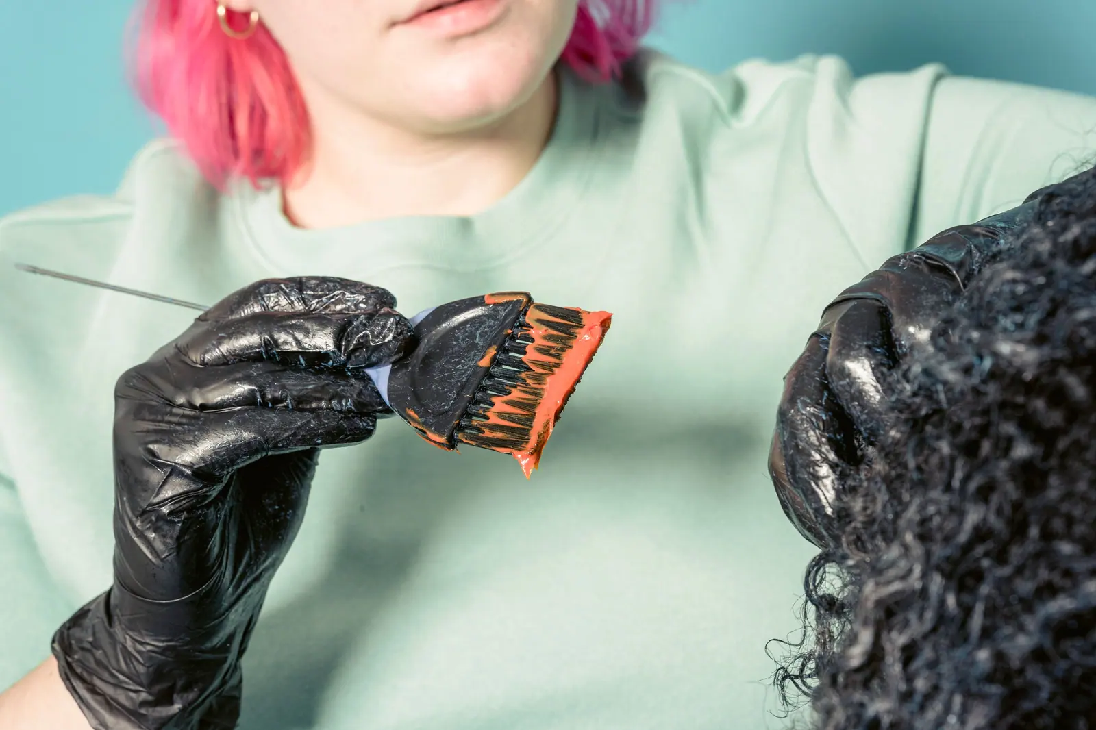 Close-up of a hairstylist dyeing curly hair in a salon environment.