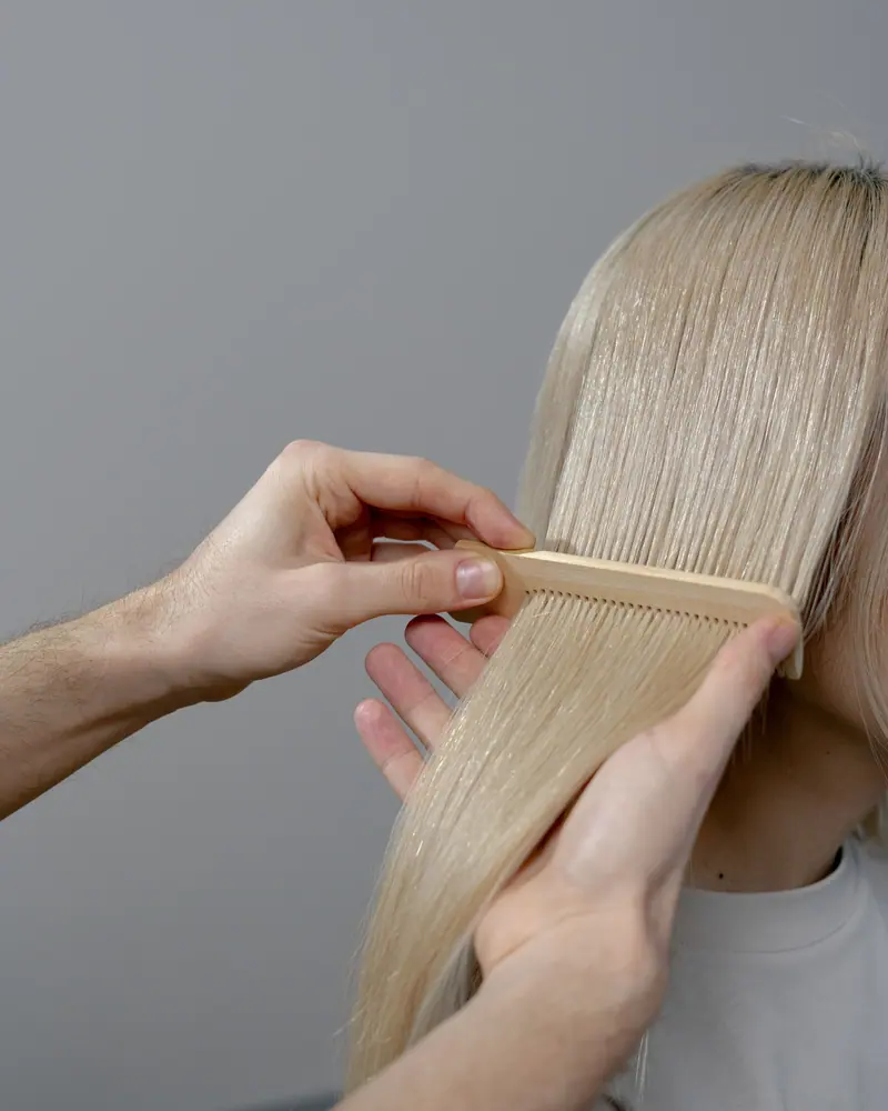 Close-up of a hairstylist combing blonde hair, showcasing attention to detail.