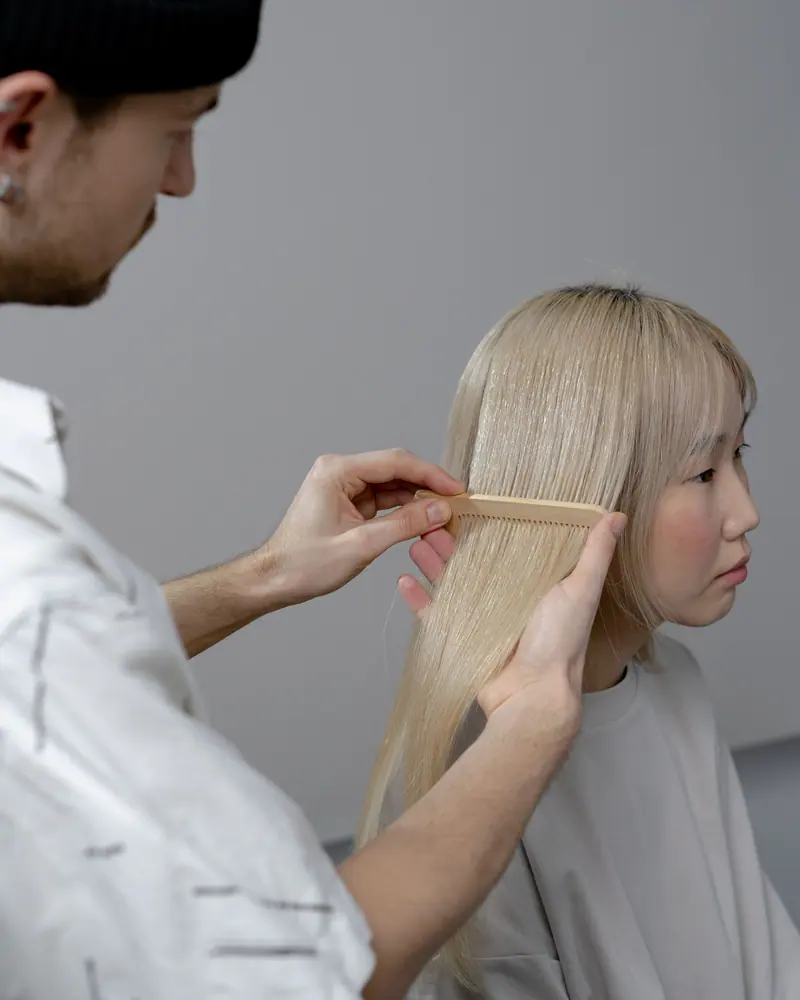 Close-up of hairstylist combing blonde hair in an indoor salon setting, focusing on haircare.