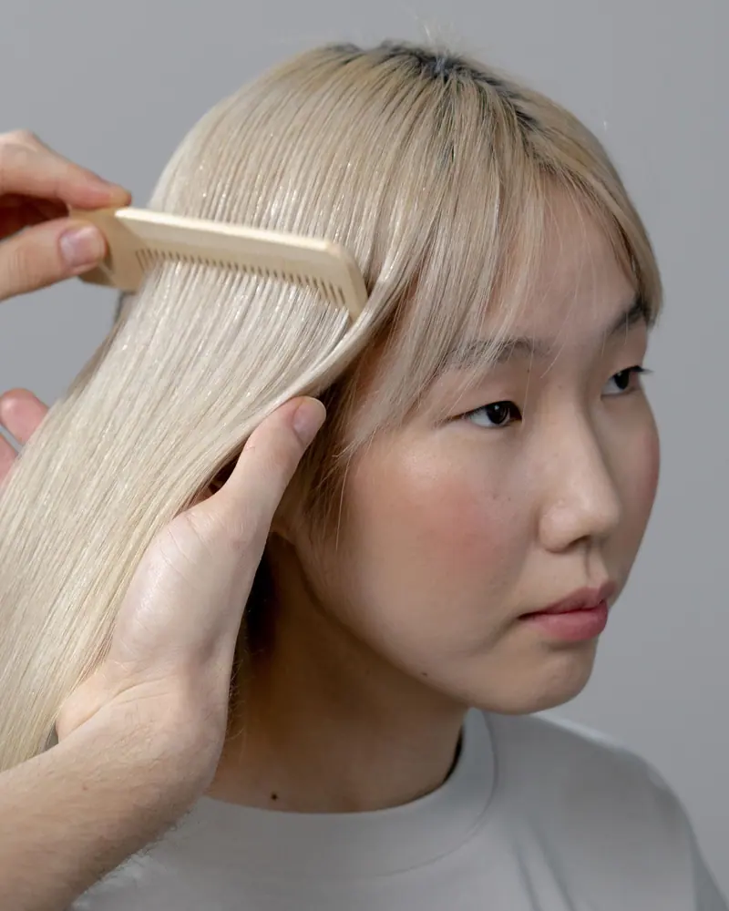 Hairstylist carefully combs blonde woman's hair in a salon setting, focusing on precision.