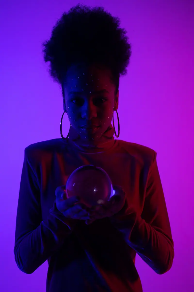 A woman with afro hair holding a crystal ball in a purple-hued studio setting, exuding a mystical vibe.