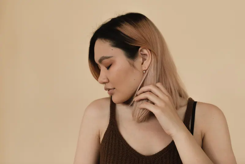 Portrait of an Asian woman with colored hair, eyes closed, posing against a beige background in a studio.