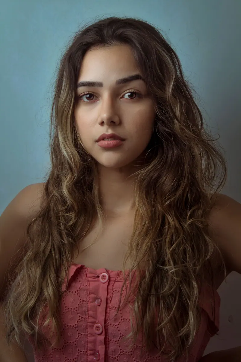 Captivating portrait of a young woman with long wavy hair against a soft blue background.