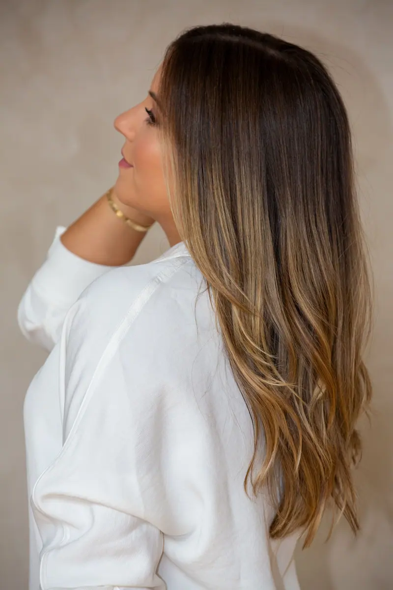 Stylish side view portrait of a woman with long brunette hair wearing a white shirt.
