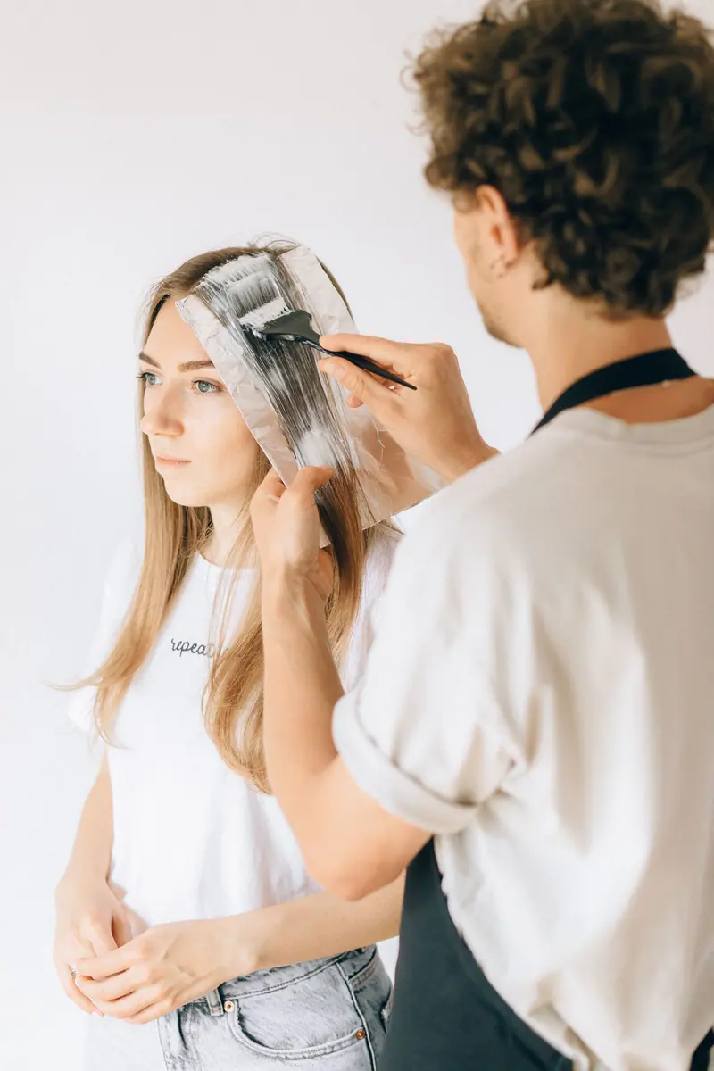 A hairstylist applying hair dye to a customer's hair in a salon, showcasing modern self-care.