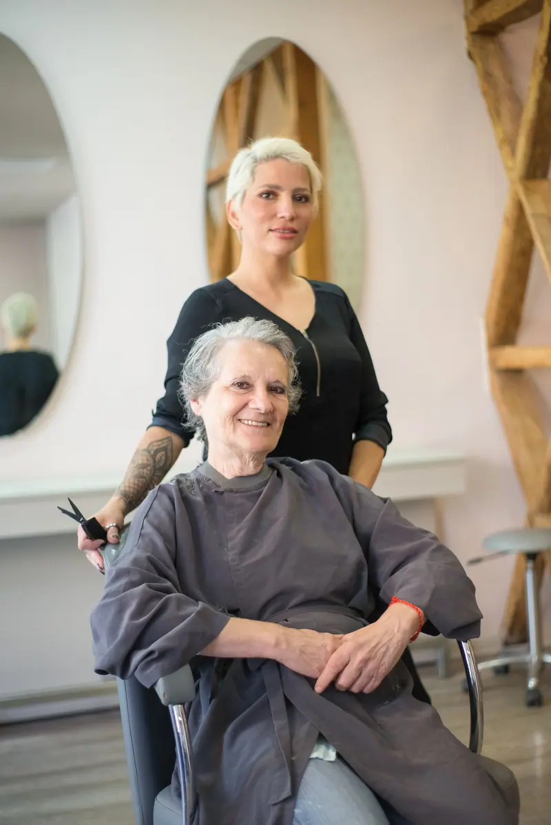 Elderly woman enjoys haircut with smiling stylist at a salon in Portugal.