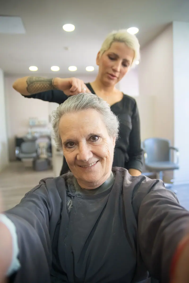 Smiling senior woman with hairdresser in a salon. A joyful hair styling session indoors.