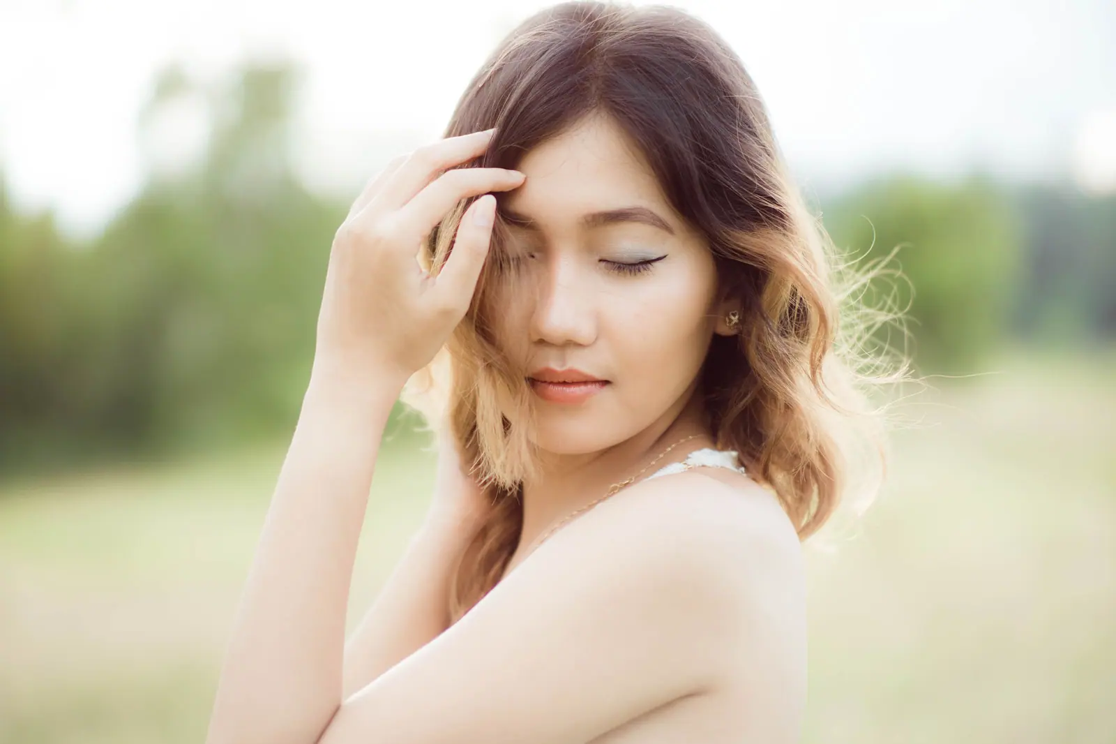 Woman with soft caramel balayage waves touching her hair in a sunlit meadow