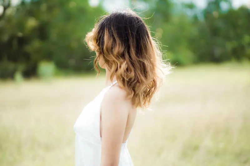 A woman with wavy blonde hair stands in a sunlit meadow, capturing a serene summer vibe.