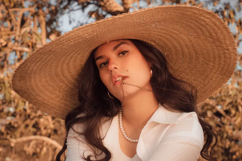 Fashionable portrait of a woman in a straw hat and pearls, exuding rustic elegance.