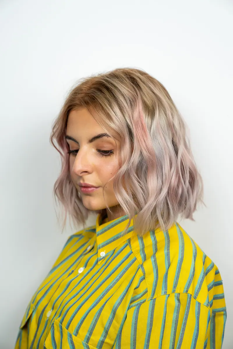 Profile portrait of a young woman with pastel blonde hair wearing a vibrant striped shirt.