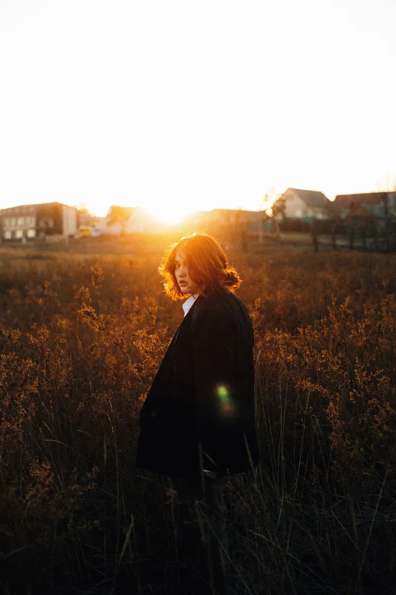 A woman stands in a field during sunset, casting a warm glow around her in an autumn landscape.