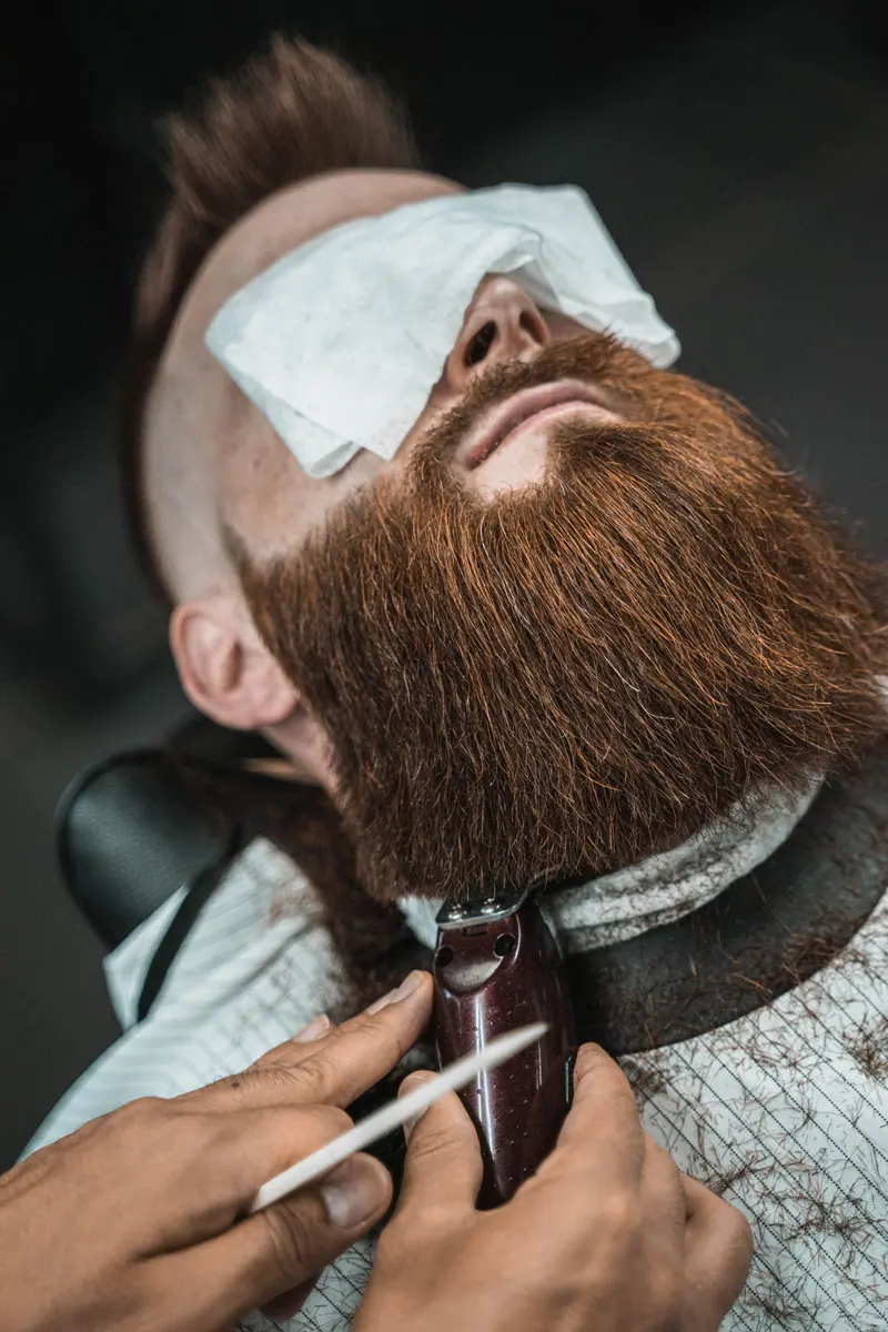 Close-up of a man's beard being trimmed by a barber in a barbershop setting.