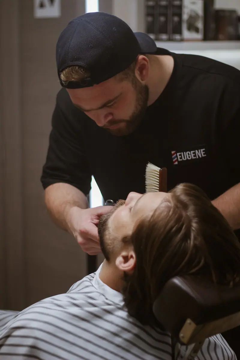 Barber trimming a beard under warm light