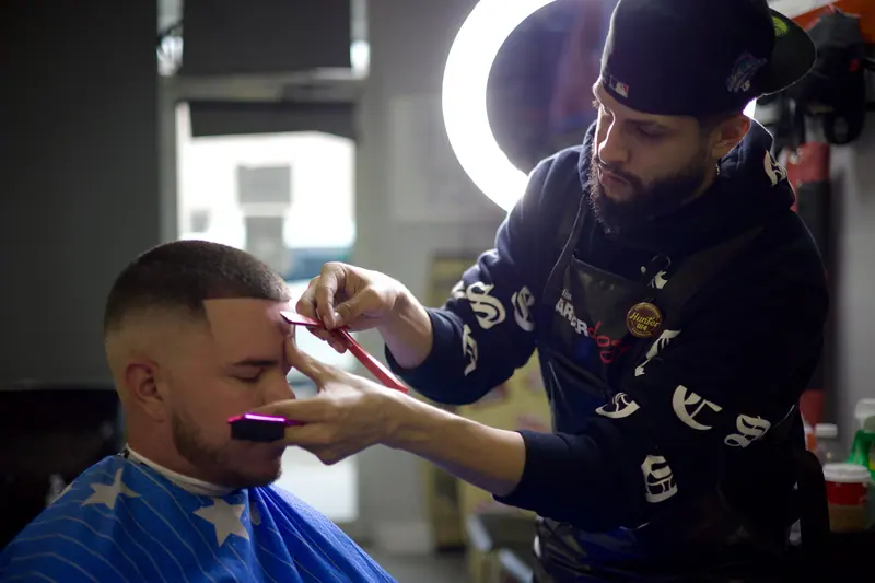Barber performing precise haircut with focused attention in modern barbershop setting.